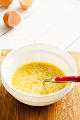 Mixing ingredients for paleo pancakes in white bowl - eggs, mashed banana on white rustic wooden background.  Close up