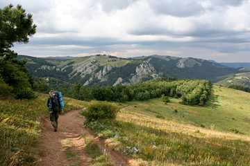 Fototapeta na wymiar The man with the backpack go on the path in mountains on the summer sunny day. This photo was taken in Crimean Mountains, on South Demerdzhi mountain.