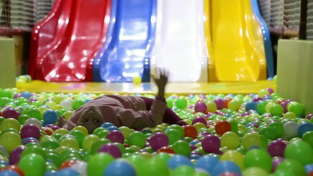 The girl lies in a pile of balls at an entertainment park, she sadly throws balls

