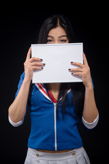 Asian woman hiding behind notebook isolated on black background. Brunette lady posing with blank poster in studio.