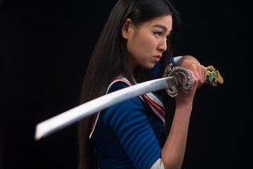 Pretty brunette lady with red lips looking like warrior. Asian lady posing sword for photographer in studio.