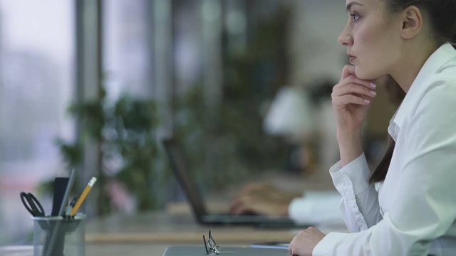 Pensive woman drumming fingers on table at laptop, thinking about new project