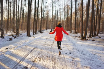 Young slender girl in a red coat runs along a snowy path in the Park, fun bouncing and waving his arms.