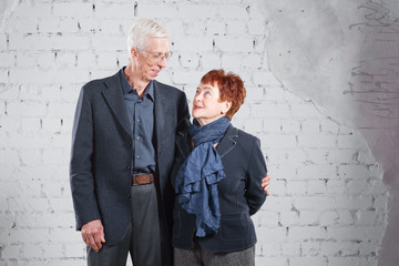 Happy smiling old couple standing cuddling together isolated on white brick background. copy space.