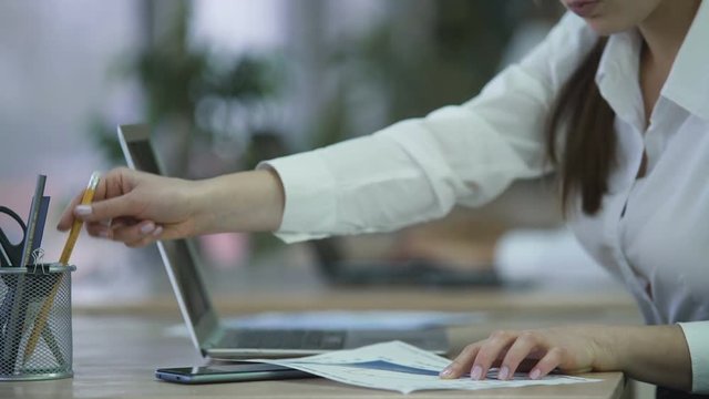 Woman inserting data on laptop from paper documents, preparing report at office