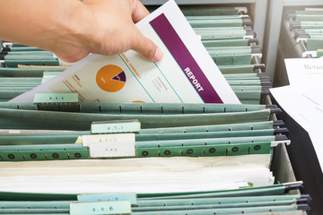 Hand holding report file in filing cabinet