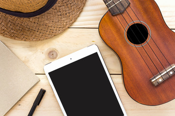 close-up ukulele, tablet computer and notebook on wood background. over light