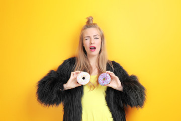 Young beautiful woman with doughnuts on yellow background