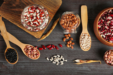 Assortment of haricot beans in bowls and spoons on dark wooden background