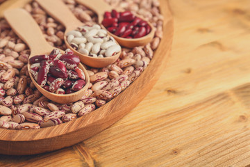 Assortment of haricot beans in spoons on wooden background