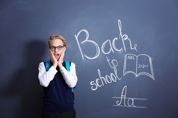 Pupil with backpack standing near school blackboard