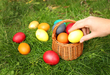 Woman hand taking Easter egg from basket on green grass