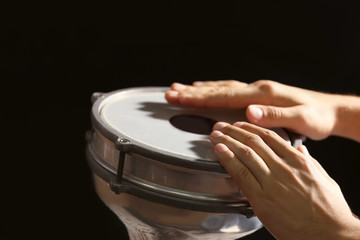 Hands of man playing African drum on dark background