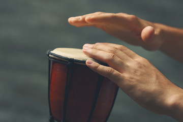 Hands of man playing African drum on blurred grey background, close up