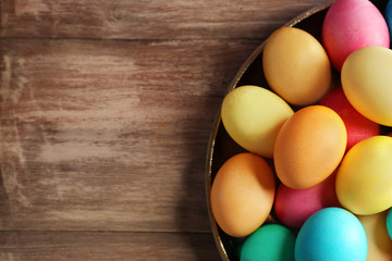 Metal dish with colorful Easter eggs on wooden table, closeup