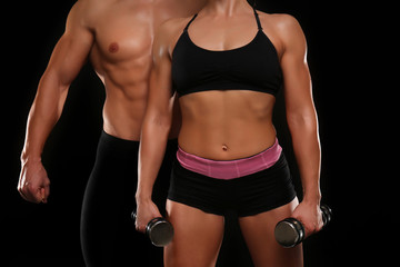 Fototapeta na wymiar Sporty young couple with dumbbells on black background, closeup