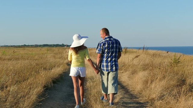 4K. Adult couple  go on  seashore, coastline in summer time. Back view