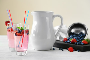 Glass of refreshing homemade drink with berries and jug on table