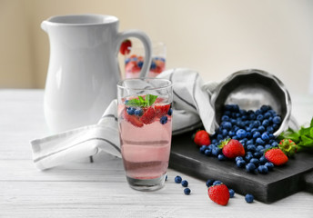 Glass of refreshing homemade drink with berries and jug on table