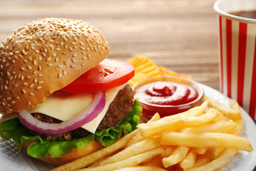 Tasty burger with snacks and coke on wooden table
