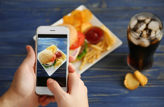 Female hands taking photo of tasty burger with snacks on table