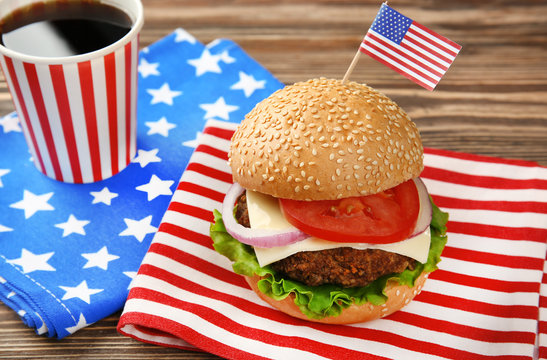 Tasty burger with coke and American flag on table