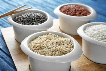 Different types of rice in bowls on wooden tray closeup