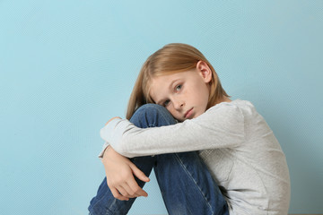 Upset girl sitting on blue wall background