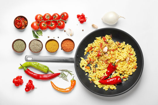 Cooked rice in pan and vegetables with spices on white background
