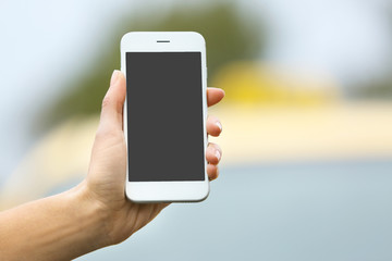 Woman ordering taxi by cellphone on blurred car background