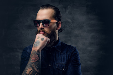 Thoughtful bearded male in sunglasses with tattoos on his arms.