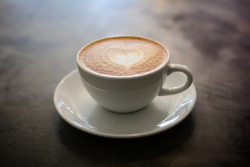 Hot coffee with heart make up on face of milk cream in white cup on vintage table background.