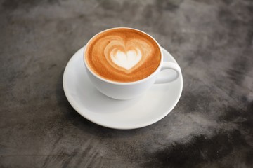 Hot coffee with heart make up on face of milk cream in white cup on vintage table background.