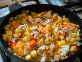 Picture of the frying colourful meal in the frying pan close up. Background like pattern. Black frying pan on a white gas stove.