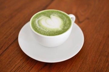 Hot matcha green tea in white cup on wood table.