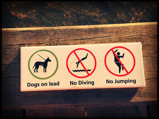Warning sign on a wooden pier - dogs on lead, no diving, no jumping. Vintage look and feel