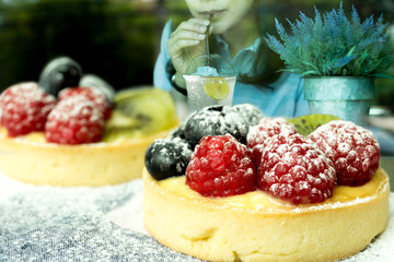 Fresh fruit tart cakes with woman drinking juice with lemon in t