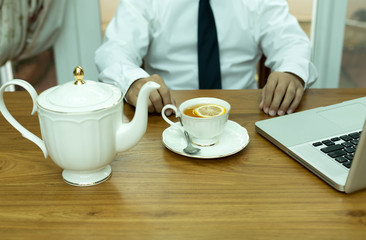Businessman sitting in office with cup of tea and lemon and lapt