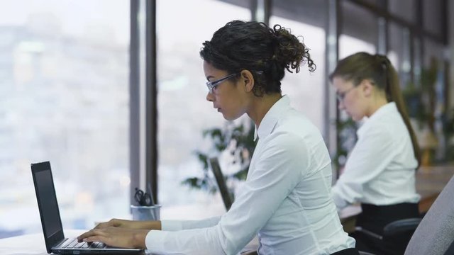 Mixed race business woman making notes, typing on laptop, hard-working manager
