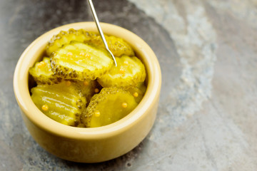 Fresh homemade pickled cucumber with mustard seeds in small ceramic bowl. Small fork stuck in one slice.