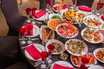 round table decorated with red wine glasses, a black tablecloth and italian dishes