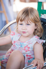 Fototapeta premium portrait of three years old blonde pretty girl with dress sitting on a chair and looking side 