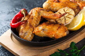 Grilled chicken wings on a cast iron pan on a black oval stone background. Selective focus.