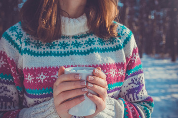 Woman holds cup of coffee with marshmallow in winter forest