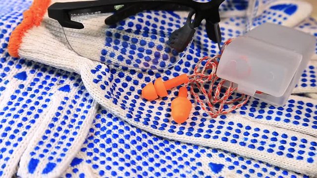 Thin work gloves with  blue pimples, protective glasses and ear plugs on a rotating surface, Personal protective equipment background. Industrial safety concept.