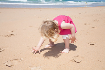 Fototapeta na wymiar little girl crouch and writing with finger on sand beach