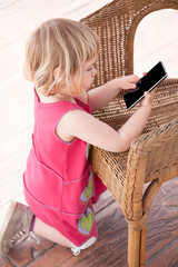little girl kneeling using mobile phone on wicker chair