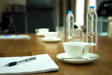 Cup of coffee with pens and paper on wooden table in conference