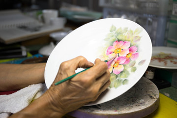 Old woman hand painting flower on ceramic plate