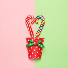 Top view of a colorful candy cane in a heart shape on a pastel pink and green background. Minimal style